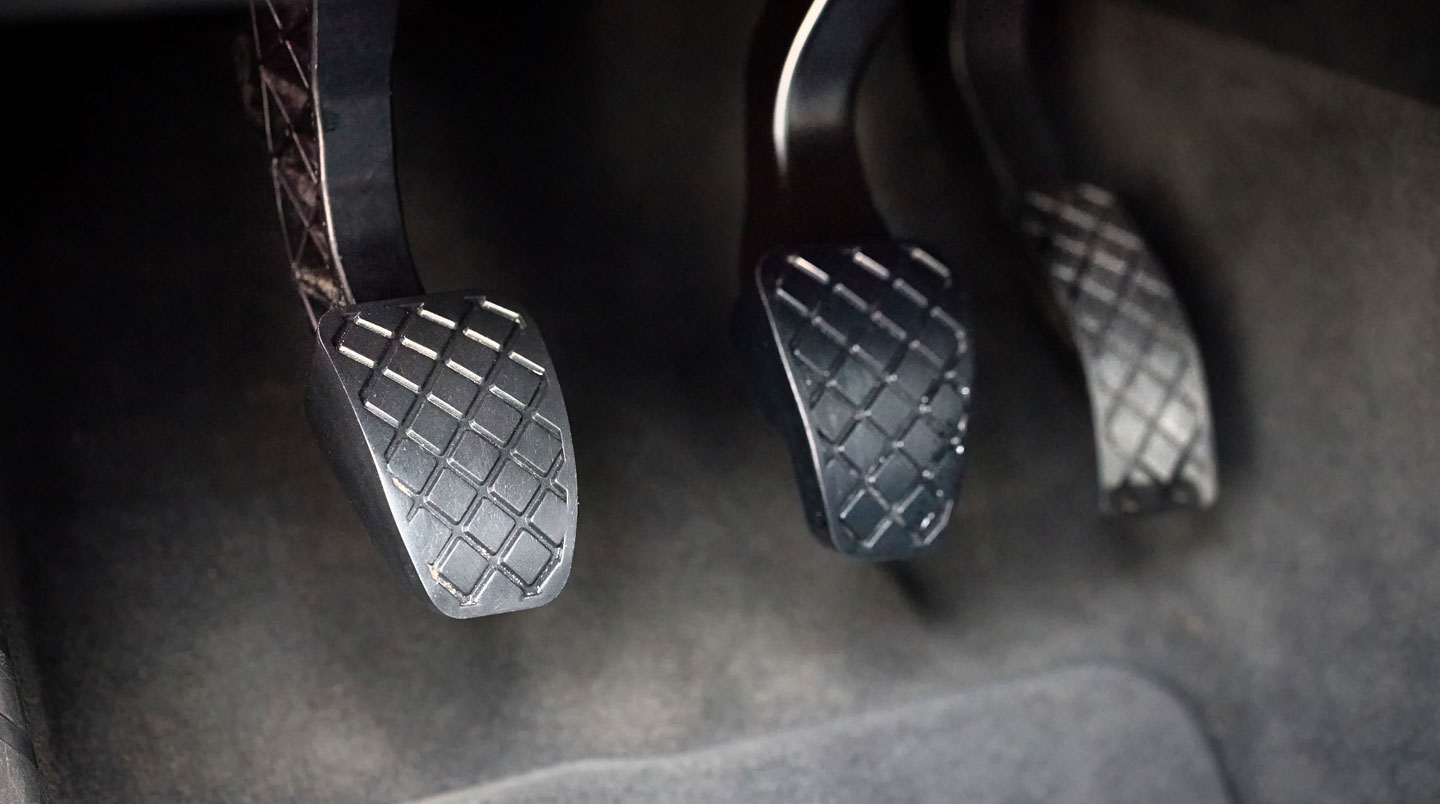 Vue du pédalier d'une voiture de collection avec pied sur la pédale d'embrayage